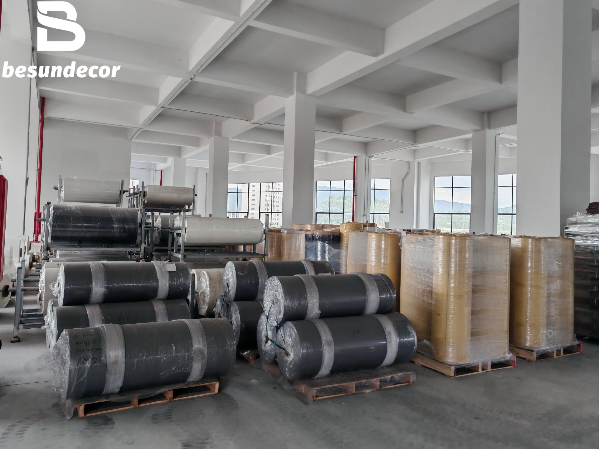 BESUN DECOR warehouse interior — rolls of decorative film and flat-stacked ASA sheet on pallets